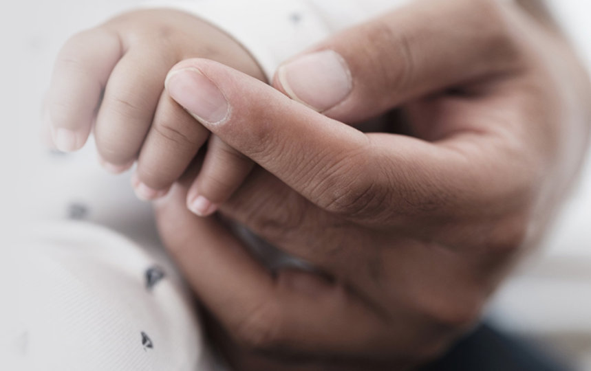 An adult hand holding a baby’s hand.