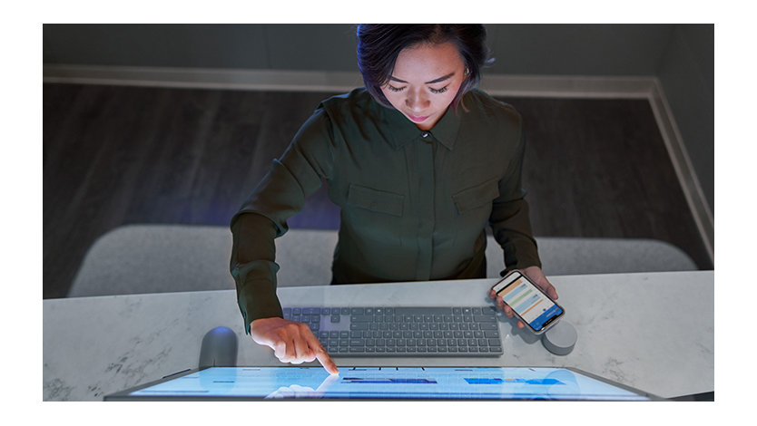 A woman holding a phone in one hand uses a touchscreen monitor with the other.