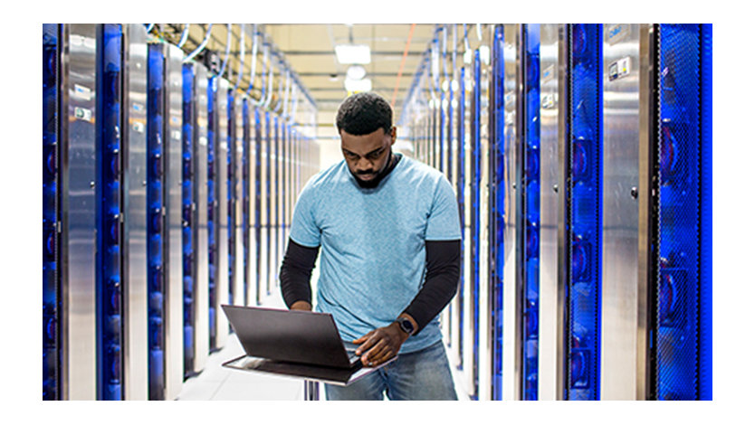 A man stands at his laptop in a server room.