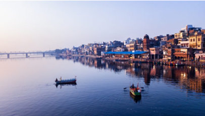 Two small boats on a lake in front of a city, with a bridge in the distance.