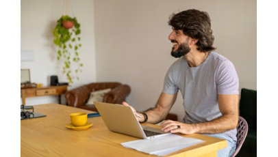 Young business man working at home in his kitchen with laptop and papers on kitchen wooden desk.