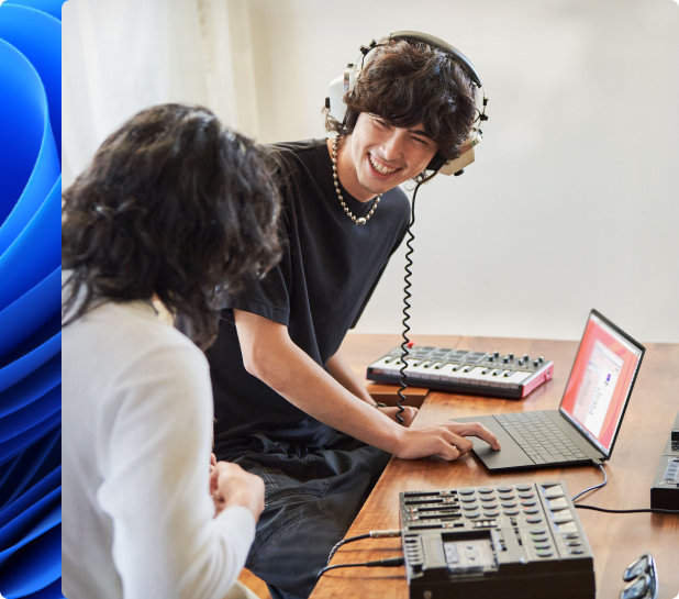 Ung mand, der smiler og bærer hovedtelefoner, og en anden person, der laver musik på en laptop med et elektronisk tastatur