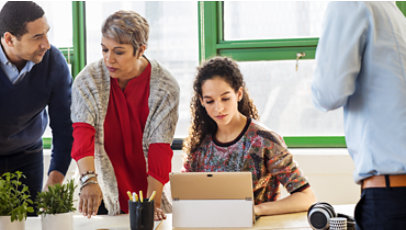 A woman works on a laptop seated next to two businesspeople having a discussion.