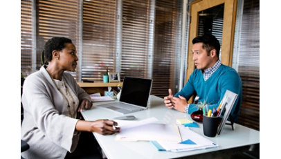 A woman and a man talking in her office with a laptop on the desk.