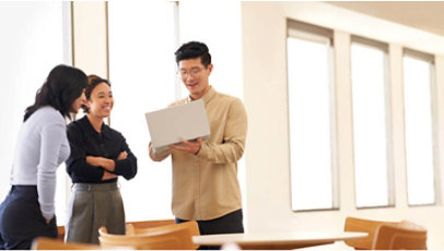 Three employees stand around a laptop computer in a bright office setting.